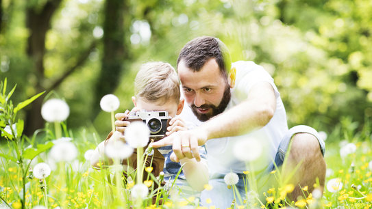 Vater und Sohn entdecken mit einer Kamera die Natur und Blumen auf Wiesen und Felder